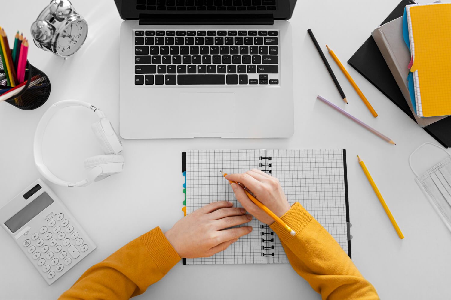 A woman's hand is writing on a notebook while sitting at a desk with a laptop, engaged in seller central management for her business.