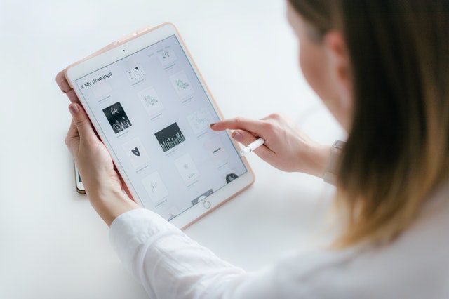 A woman using an iPad on a white table for marketplace research.