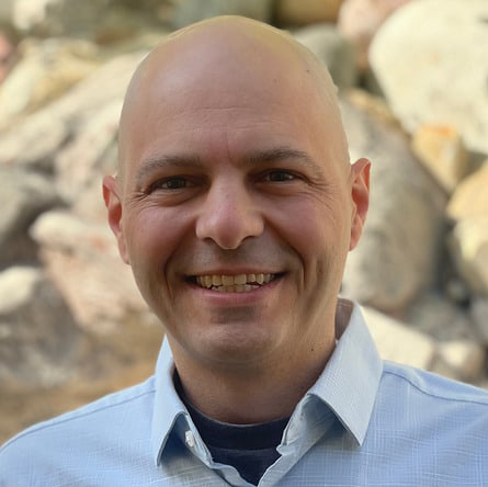 A bald man from My Amazon Guy, smiling in front of rocks.