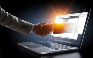 A businessman in a marketplace shaking hands with a laptop screen.