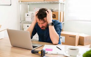 A man is sitting at a desk with a laptop in front of him, managing his Amazon Seller Central.