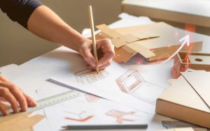 A woman is drawing on a piece of cardboard while managing her Amazon seller account.