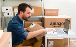 A marketing manager working on a laptop in a room full of boxes.