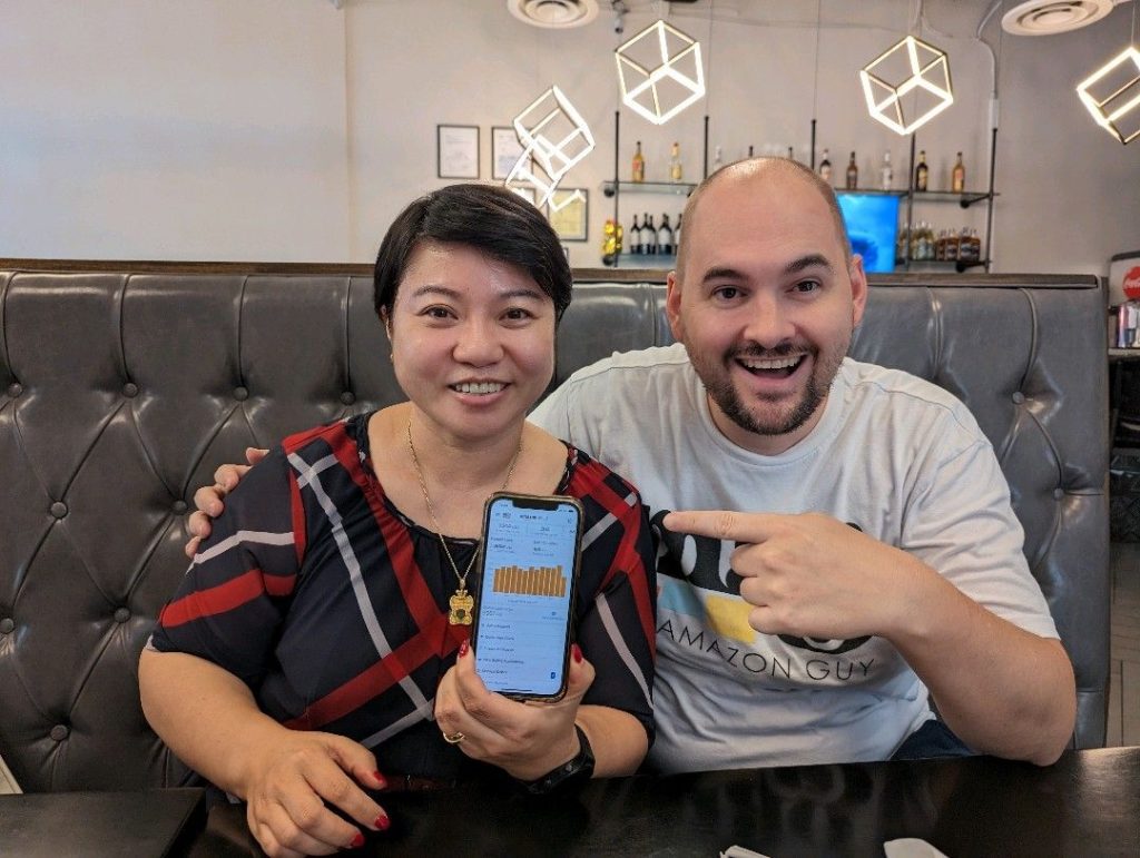 A couple posing for a photo with their phone to showcase their success in marketing management.